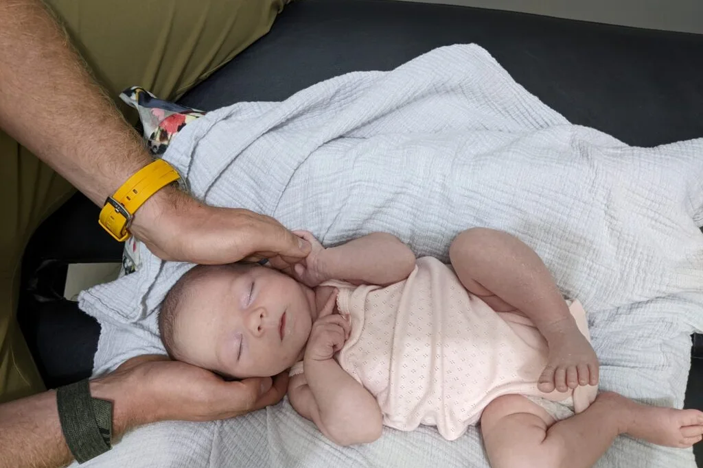 A sleeping newborn with an adult's hands supporting the head.